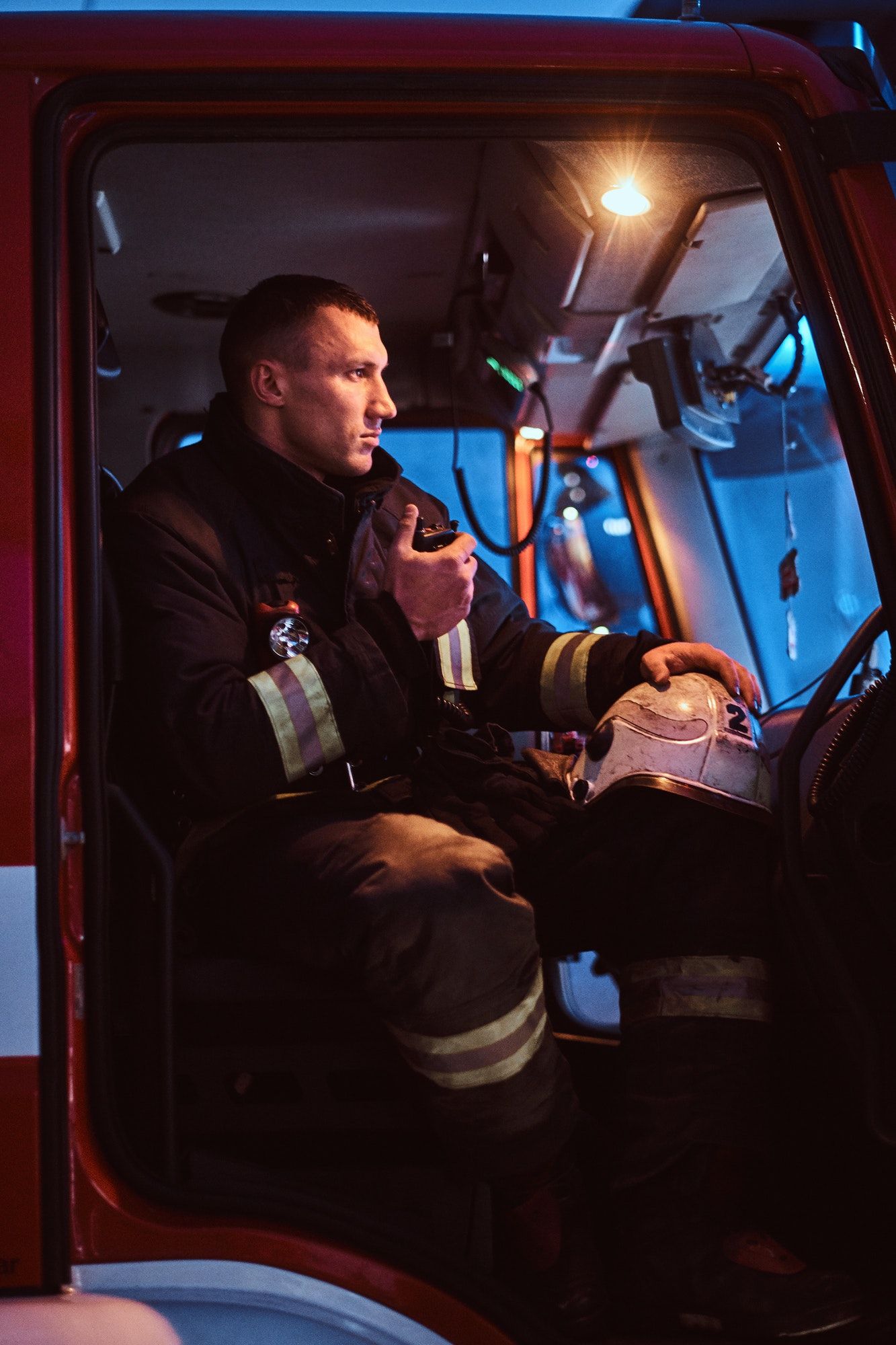Fireman wearing protective uniform standing next to a fire engine in a garage of a fire department
